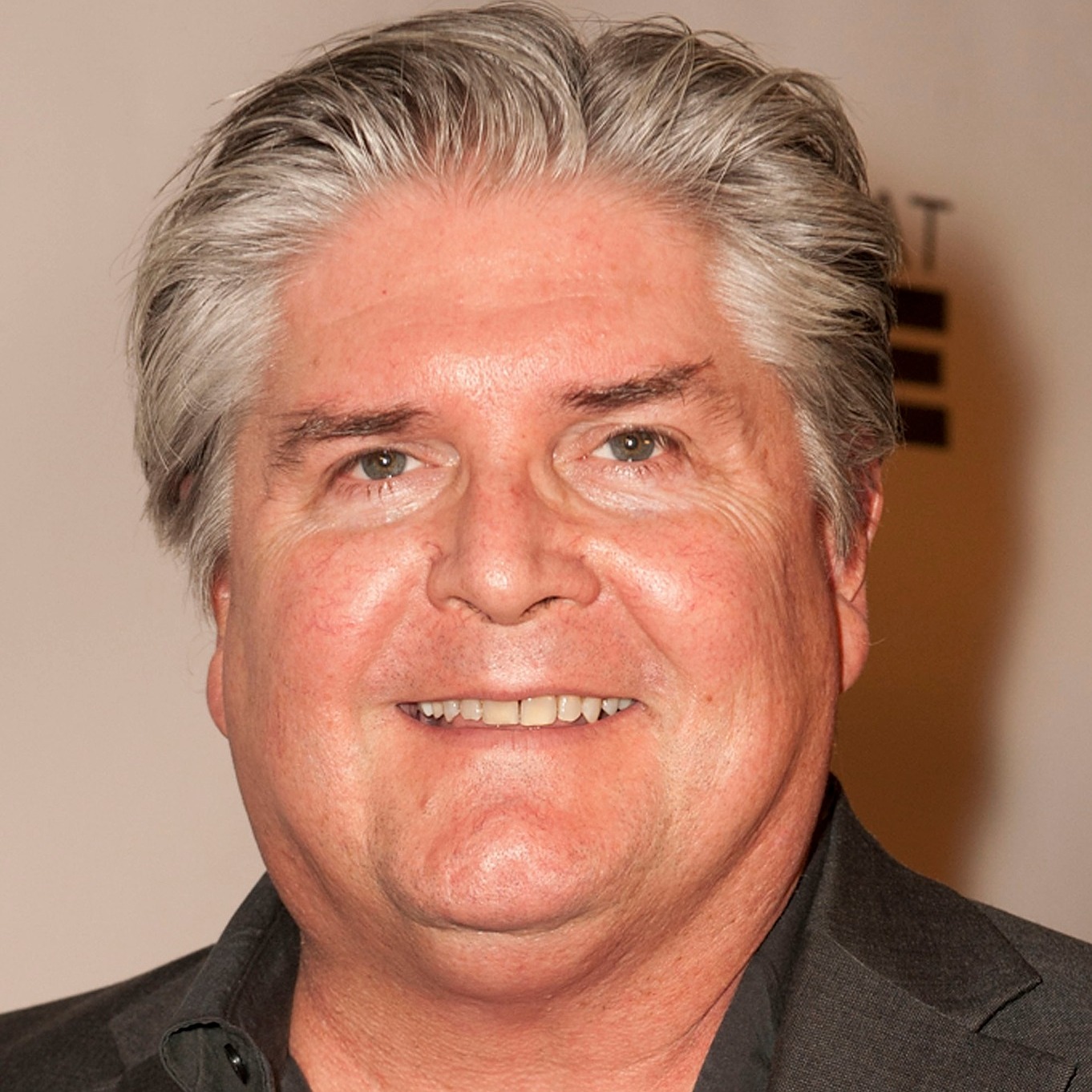 Jim Ward z&acirc;mbitor, &icirc;ntr-un sacou &icirc;nchis la culoare, pe sub care are o cămașă asortată