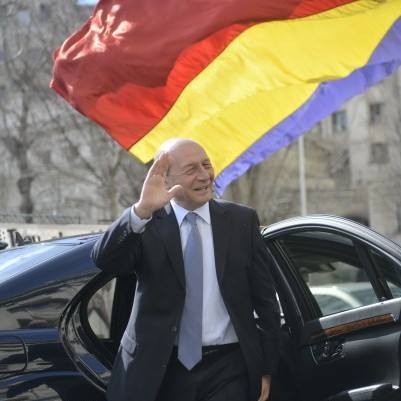 Traian Băsescu salut&acirc;nd &icirc;n timp ce coborară dintr-o mașină neagră, av&acirc;nd &icirc;n spate steagul Rom&acirc;niei