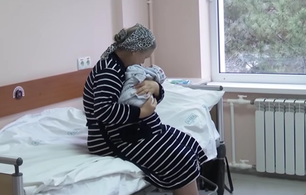 Lilia Balan la spital, &icirc;ntr-o rochie cu dungi, țin&acirc;ndu-și fetița nou-născută &icirc;n brațe