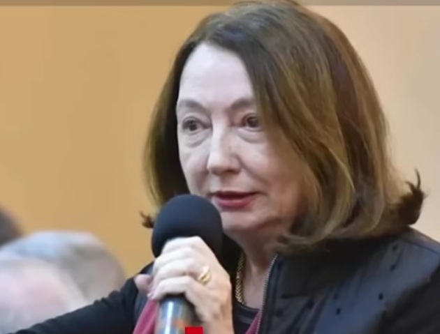 Rodica Stănoiu cu microfonul &icirc;n față și cu un inel de aur pe deget, tunsă bob și &icirc;mbrăcată &icirc;n sacou negru