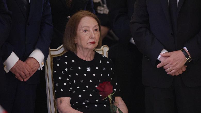 Rodica Stănoiu st&acirc;nd pe un scaun, &icirc;mbrăcată &icirc;ntr-un tricou de la Chanel, țin&acirc;nd &icirc;n m&acirc;ini un trandafir roșu