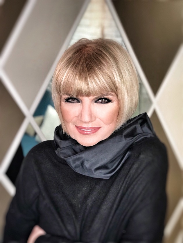 Doina Levintza zâmbitoare, cu un machiaj smokey eyes, îmbrăcată în negru, cu o eșarfă neagră la gât