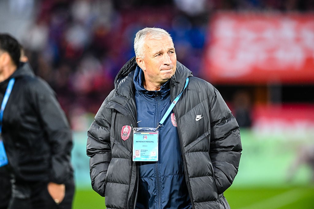 Dan Petrescu &icirc;ng&acirc;ndurat, pe marginea terenului de fotbal, purt&acirc;nd o geacă negră și lungă peste treningul bleumarin și țin&acirc;ndu-și m&acirc;inile &icirc;n buzunar