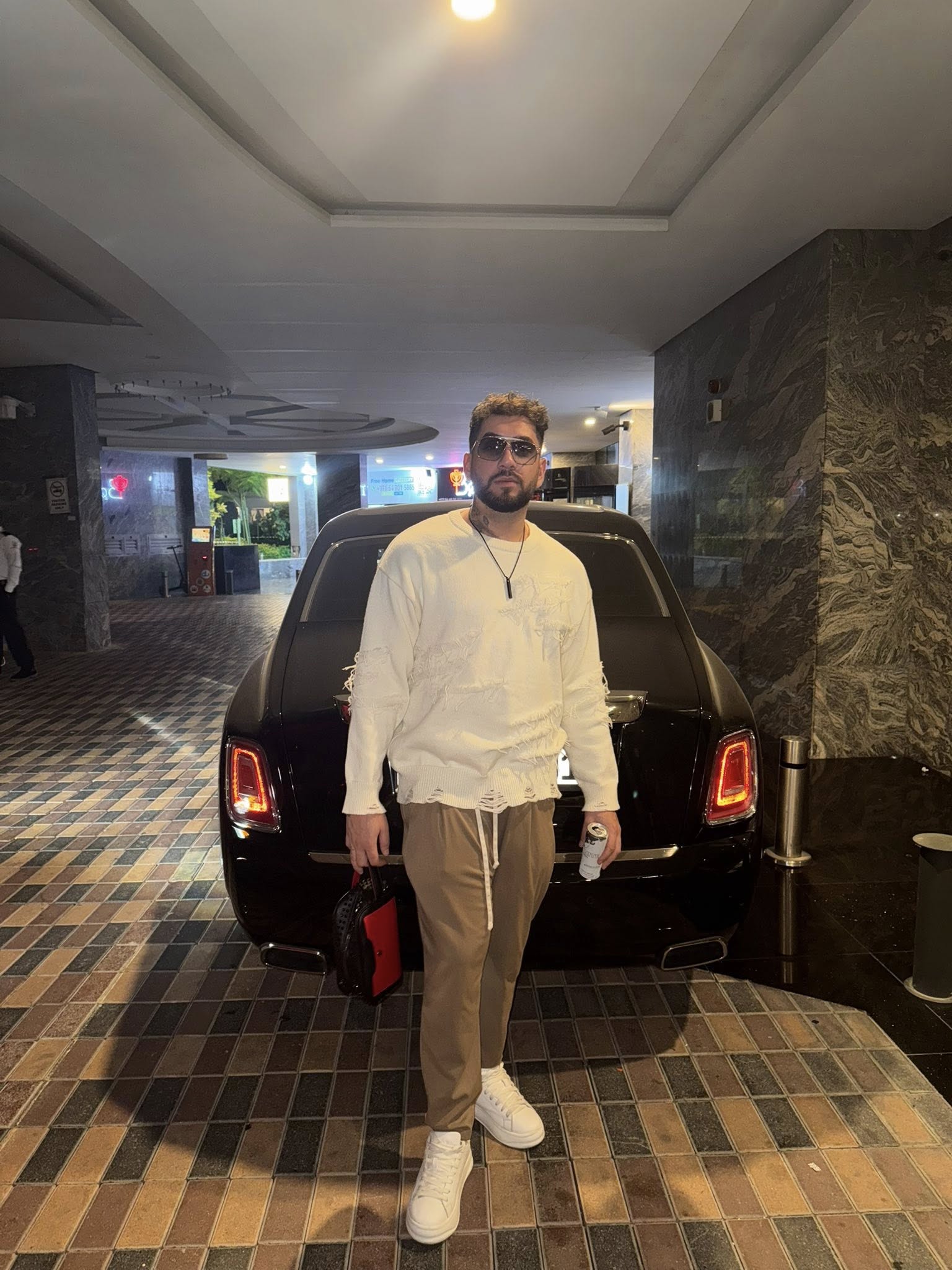 Fulgy, fiul Clejanilor, într-o parcare din Dubai, stând lângă o mașină, cu ochelarii de soare la ochi