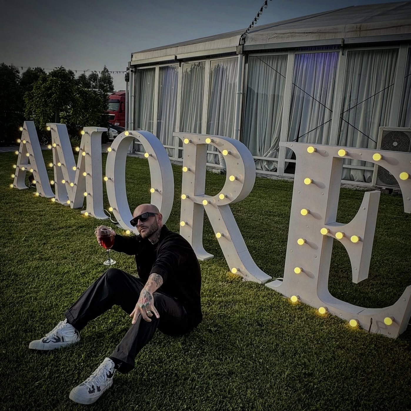 Cătălin Bordea st&acirc;nd pe gazon &icirc;n curtea unui restaurant, l&acirc;ngă un cuv&acirc;nt realizat din litere luminoase, țin&acirc;nd un pahar de vin &icirc;n m&acirc;nă