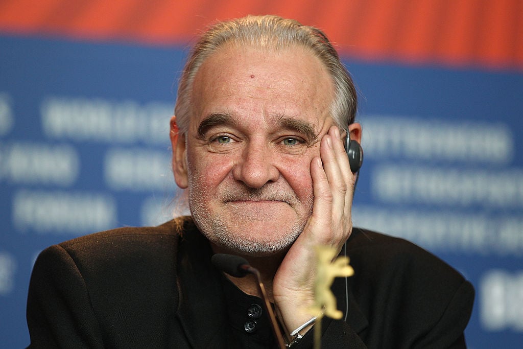 Regizorul Bela&nbsp;Tarr z&acirc;mbitor și senin, st&acirc;nd la un pupitru, &icirc;n fața unui public, cu microfonul &icirc;n față, susțin&acirc;ndu-și capul cu m&acirc;na &icirc;n care &icirc;și sprijină bărbia