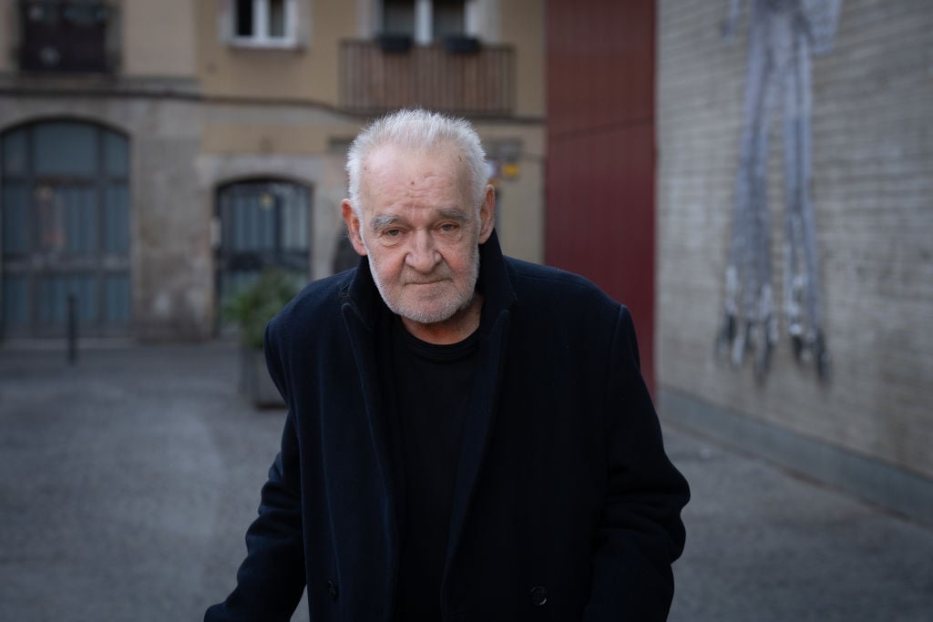 Regizorul Bela&nbsp;Tarr pe stradă, &icirc;n dreptul unor clădiri vechi, &icirc;mbrăcat complet &icirc;n negru, vizibil &icirc;mbătr&acirc;nit și slăbit