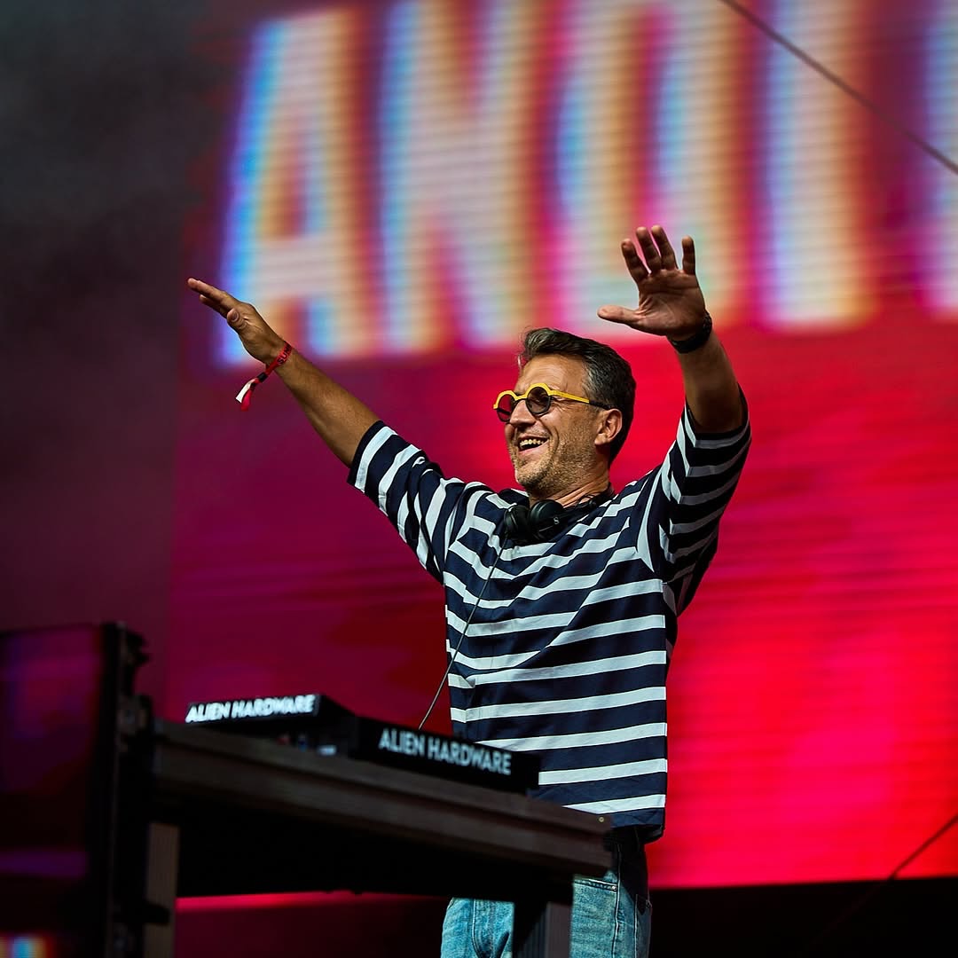 Andi Moisescu &icirc;n rol de DJ, pun&acirc;nd muzică la un eveniment, &icirc;mbrăcat &icirc;n blugi și tricou &icirc;n dungi albe și bleumarin