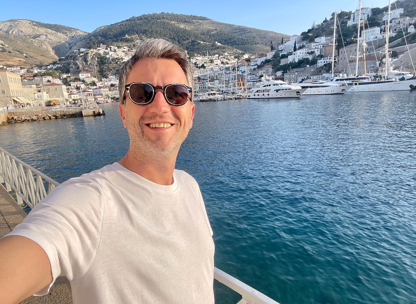 Andi Moisescu z&acirc;mbitor, făc&acirc;ndu-și un selfie pe malul mării, &icirc;n port, &icirc;n timp ce era &icirc;mbrăcat &icirc;n tricou alb și purta ochelari de soare