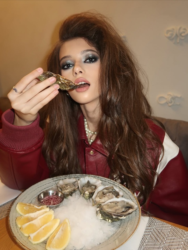 Mihaela Albu cu un look dramatic, machiată cu nuanțe &icirc;nchise, cu o coafură cu mult volum, st&acirc;nd la masa unui restaurant și m&acirc;nc&acirc;nd fructe de mare