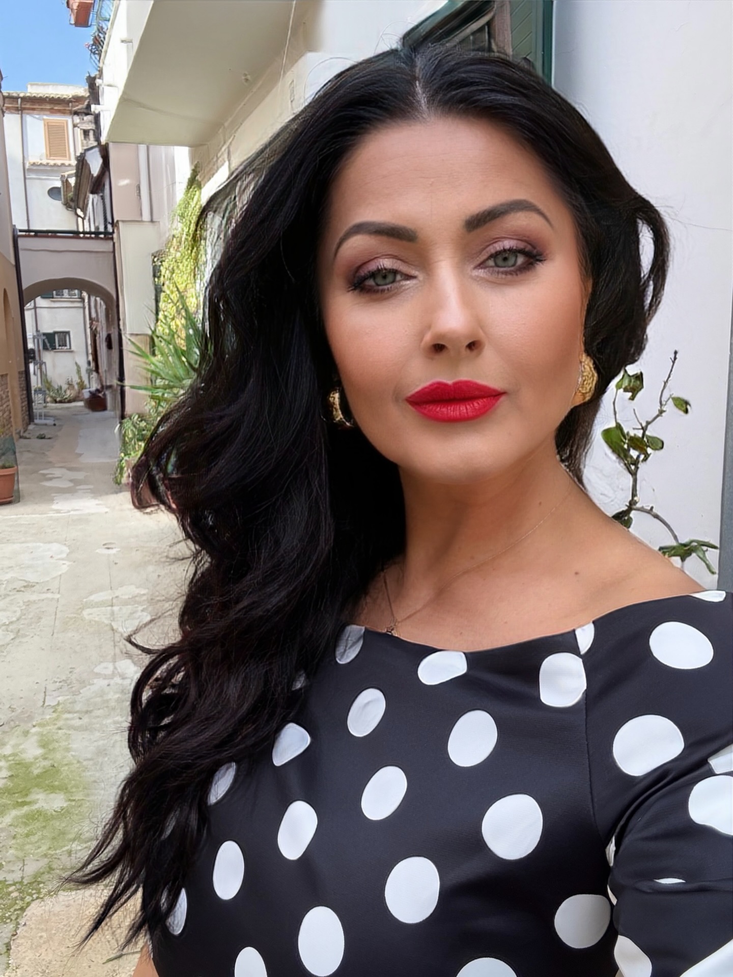 Gabriela Cristea făc&acirc;ndu-și un selfie &icirc;ntr-o rochie cu buline, cu părul lung pe spate, machiată elegant, cu ruj roșu pe buze și cercei aurii &icirc;n urechi