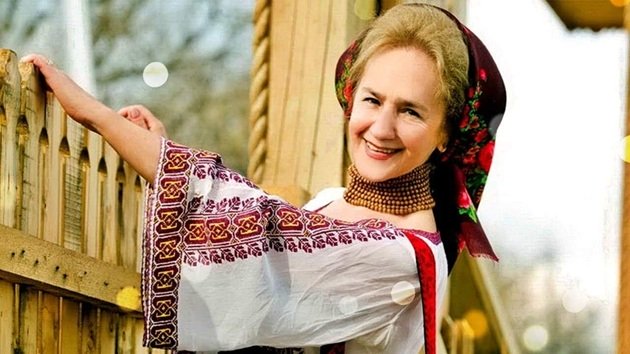 Sofia Vicoveanca z&acirc;mbitoare, &icirc;n costum popular, țin&acirc;ndu-se cu m&acirc;na de un gard de lemn, purt&acirc;nd la g&acirc;t un colier masiv din mărgele