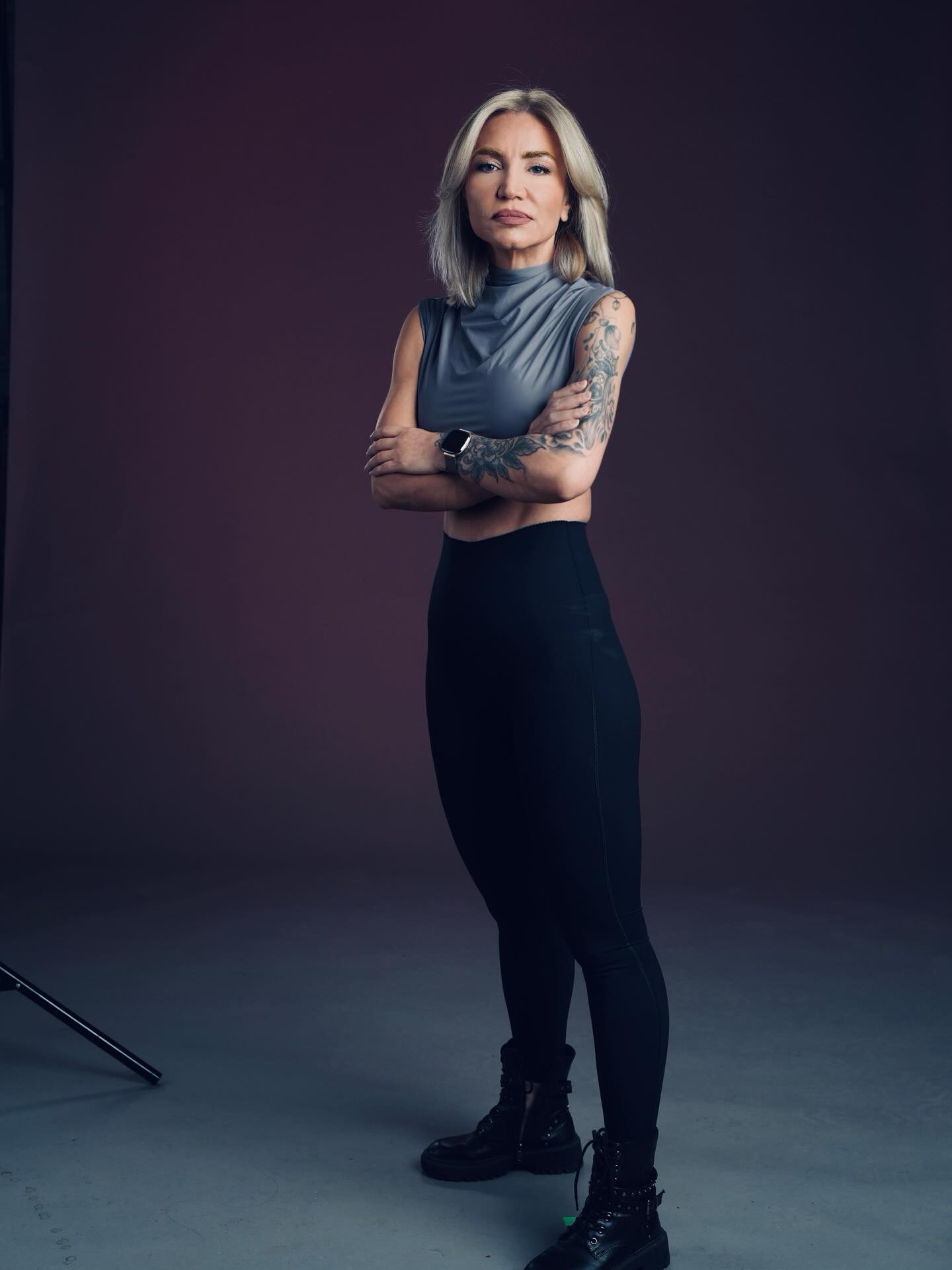 Larisa Uță &icirc;mbrăcată &icirc;n pantaloni negri cu talie &icirc;naltă și top scurt, gri, st&acirc;nd cu m&acirc;inile &icirc;ncrucișate