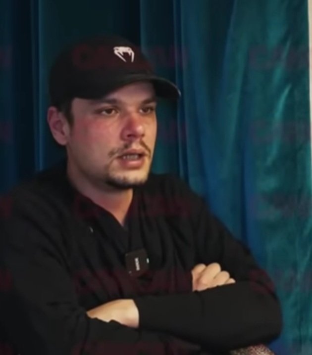 Mario Iorgulescu &icirc;mbrăcat &icirc;n negru, cu șapcă pe cap, st&acirc;nd pe scaun, l&acirc;ngă o draperie, cu m&acirc;inile &icirc;n s&acirc;n, &icirc;n timpul unui interviu acordat lui Dan Capatos