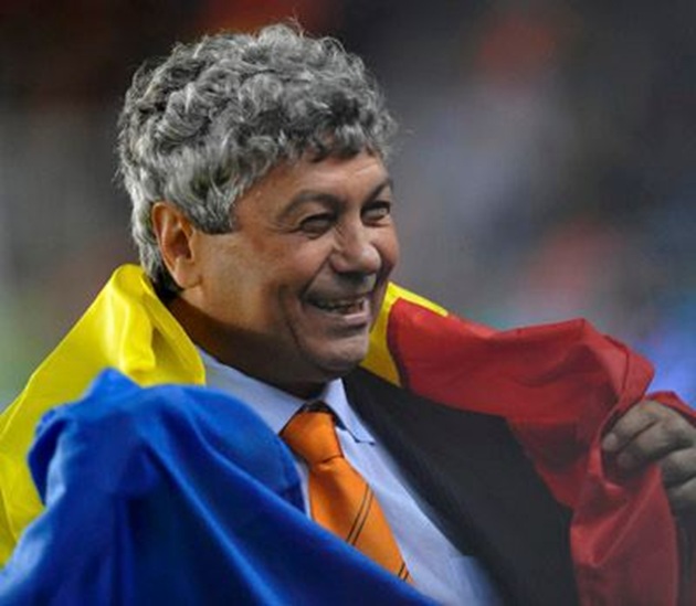 Mircea Lucescu z&acirc;mbitor, &icirc;n timpul unui meci de fotbal, purt&acirc;nd pe umeri tricolorul Rom&acirc;niei