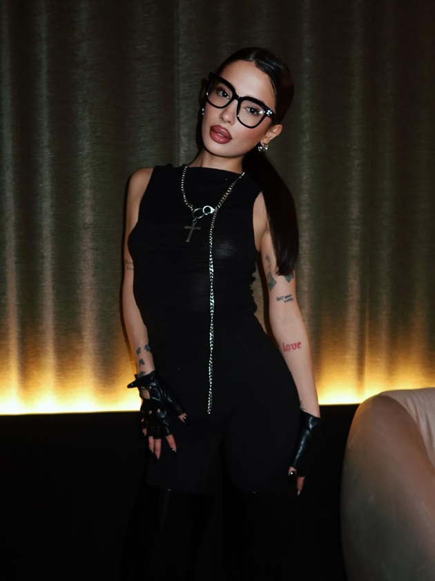 Calina Dumitrescu &icirc;ntr-un club, &icirc;mbrăcată &icirc;n negru din cap p&acirc;nă-n picioare, cu tatuaje pe brațe, cu mănuși &icirc;n m&acirc;ini, părul prins &icirc;n coadă și ochelari la ochi