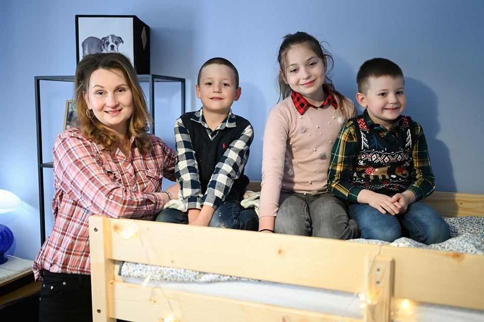 Florentina&nbsp;Filipovici z&acirc;mbitoare, alături de fata și băieții ei, care stăteau &icirc;n pat, &icirc;n dormitorul lor, după ce s-au mutat &icirc;ntr-o casă nouă, sprijiniți de Fundația Hope and Homes for Children Romania