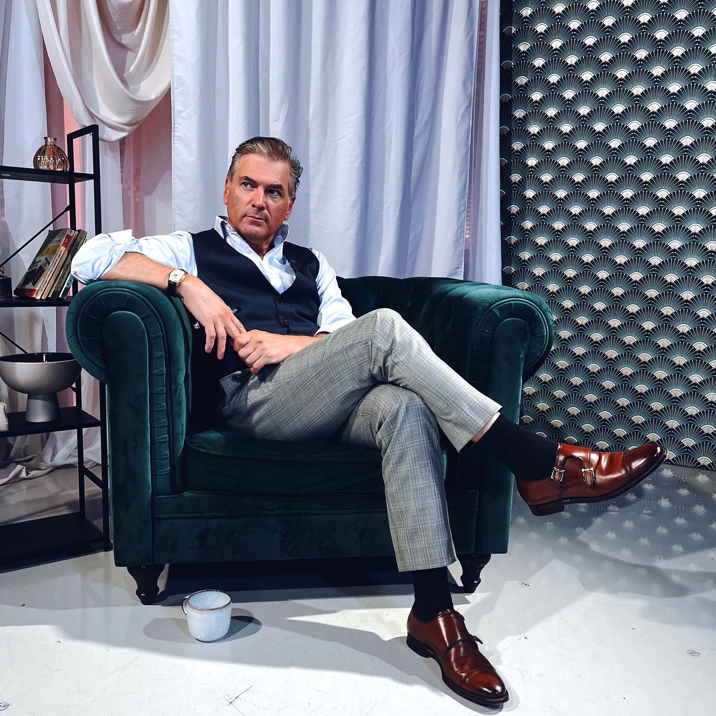 Mircea Radu st&acirc;nd picior peste picior pe un fotoliu, privind &icirc;ntr-o parte și ignor&acirc;nd camera de fotografiat