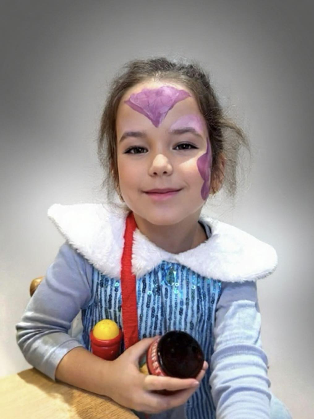 Donca, fiica Marei Bănică țin&acirc;nd &icirc;n m&acirc;nă o jucărie, &icirc;n timp ce era pictată pe față și purta o rochie cu guler de blană