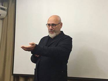 Doctorul Cristian Andrei &icirc;mbrăcat &icirc;n negru, vorbind &icirc;n fața unui public și gesticul&acirc;nd, st&acirc;nd l&acirc;ngă un ecran alb de proiector