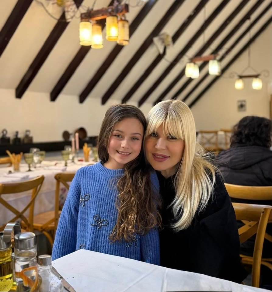 Elena Udrea &icirc;mbrățiș&acirc;nd-o pe fiica ei, Eva, care stă z&acirc;mbitoare l&acirc;ngă ea, la masa unui restaurant cu decor rustic