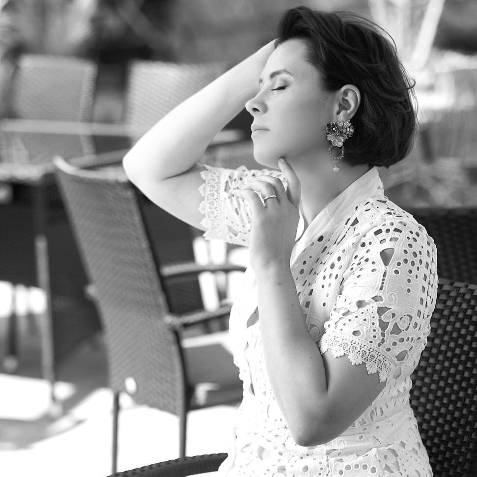 Imagine alb-negru cu Oksana Ionașcu &icirc;n rochie albă din dantelă, cu cercei mari &icirc;n urechi, st&acirc;nd &icirc;ntr-o parte, &icirc;ncadr&acirc;ndu-și fața cu m&acirc;inile