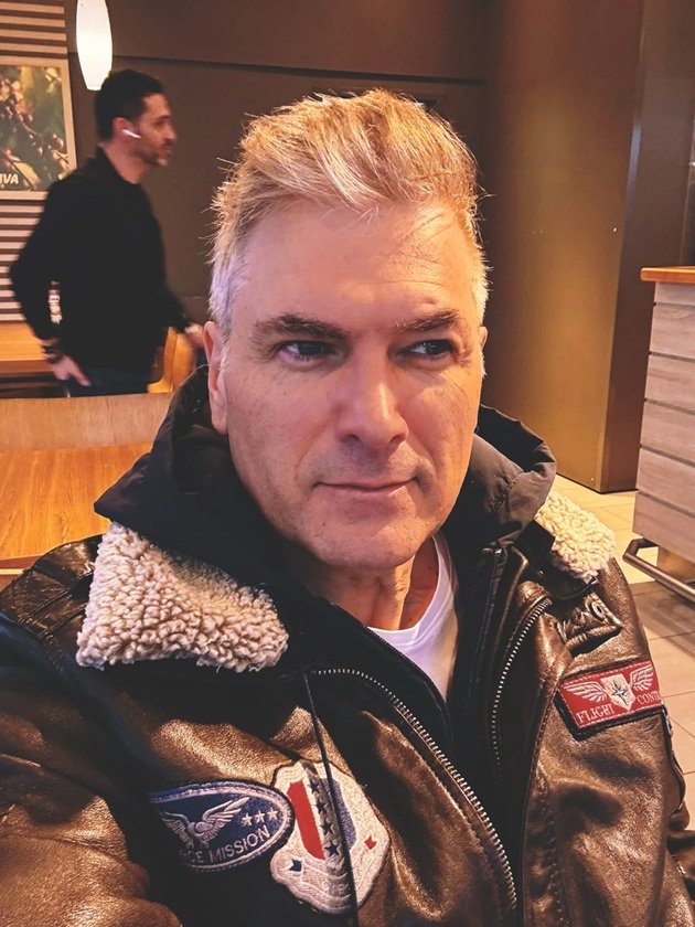 Mircea Radu făc&acirc;ndu-și un selfie &icirc;ntr-o benzinărie, &icirc;mbrăcat &icirc;n geacă neagră de piele, privind &icirc;ntr-o parte