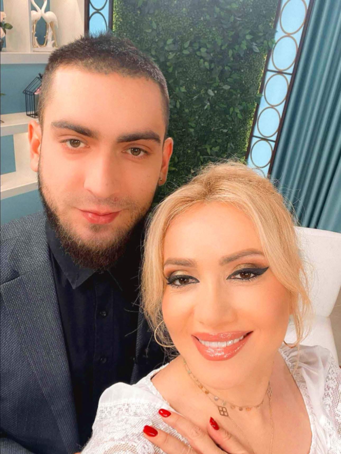 Adriana Ochișanu z&acirc;mbitoare, &icirc;mbrăcată &icirc;ntr-o ie albă din dantelă, făc&acirc;ndu-și un selfie cu fiul ei, Cristian Botgros, &icirc;mbrăcat &icirc;n cămașă neagră și sacou gri &icirc;nchis