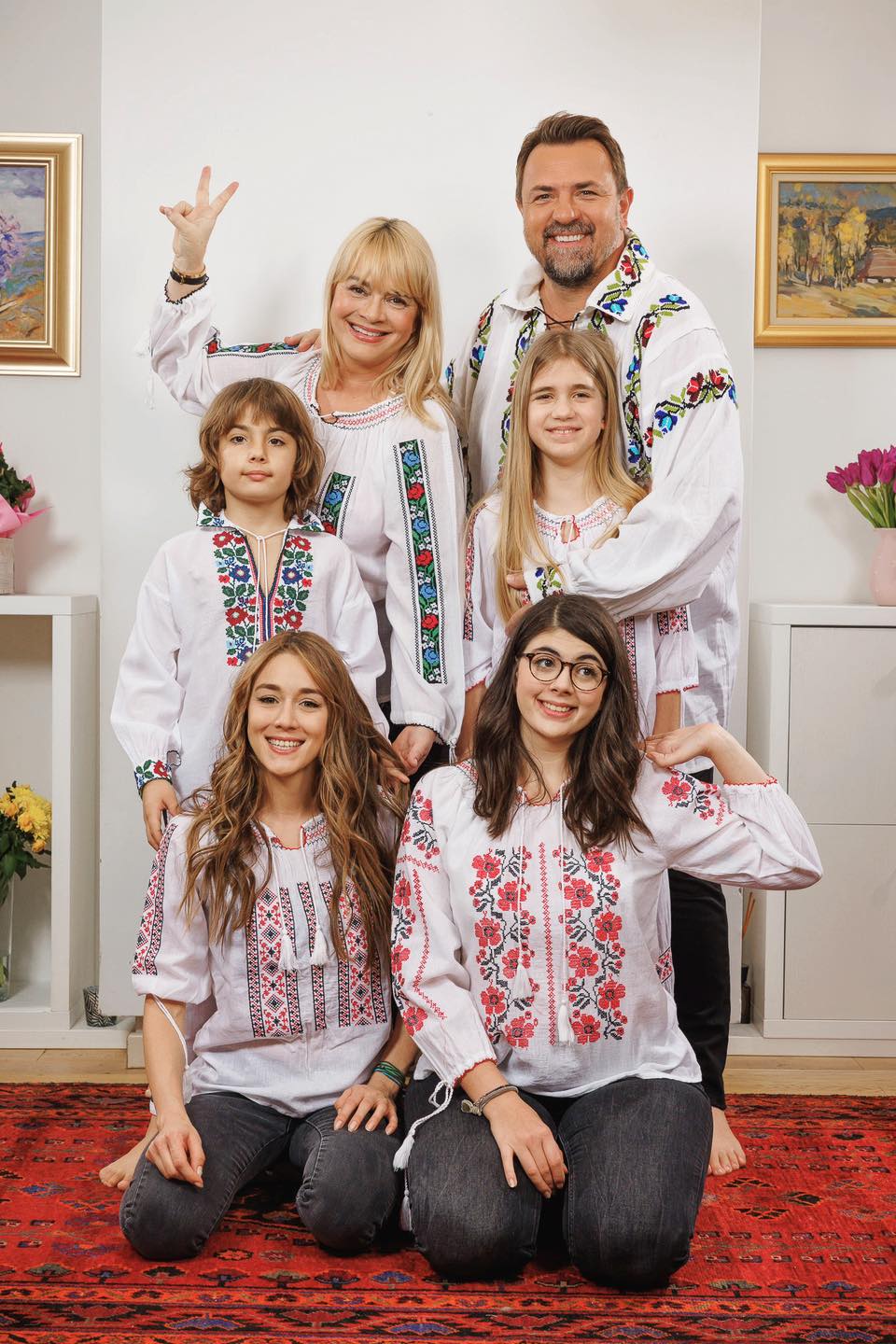 Tablou de familie cu Horia Brenciu, soția și copiii, &icirc;mbrăcați toți &icirc;n blugi și ii albe, cu motive tradiționale colorate