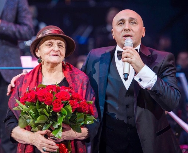 Marcel Pavel pe scenă, &icirc;n timpul unui concert, alături de mama sa, care ține &icirc;n brațe un buchet mare de trandafiri, &icirc;n timp ce erau am&acirc;ndoi &icirc;mbrăcați elegant