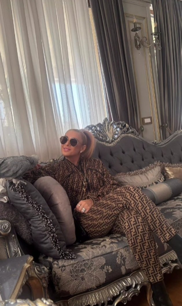 Anamaria Prodan st&acirc;nd &icirc;n casă, pe o canapea cu detalii prețioase, purt&acirc;nd ochelari de soare, &icirc;n timp ce are părul prins &icirc;n coadă și este &icirc;mbrăcată &icirc;ntr-un compleu maro cu imprimeu negru