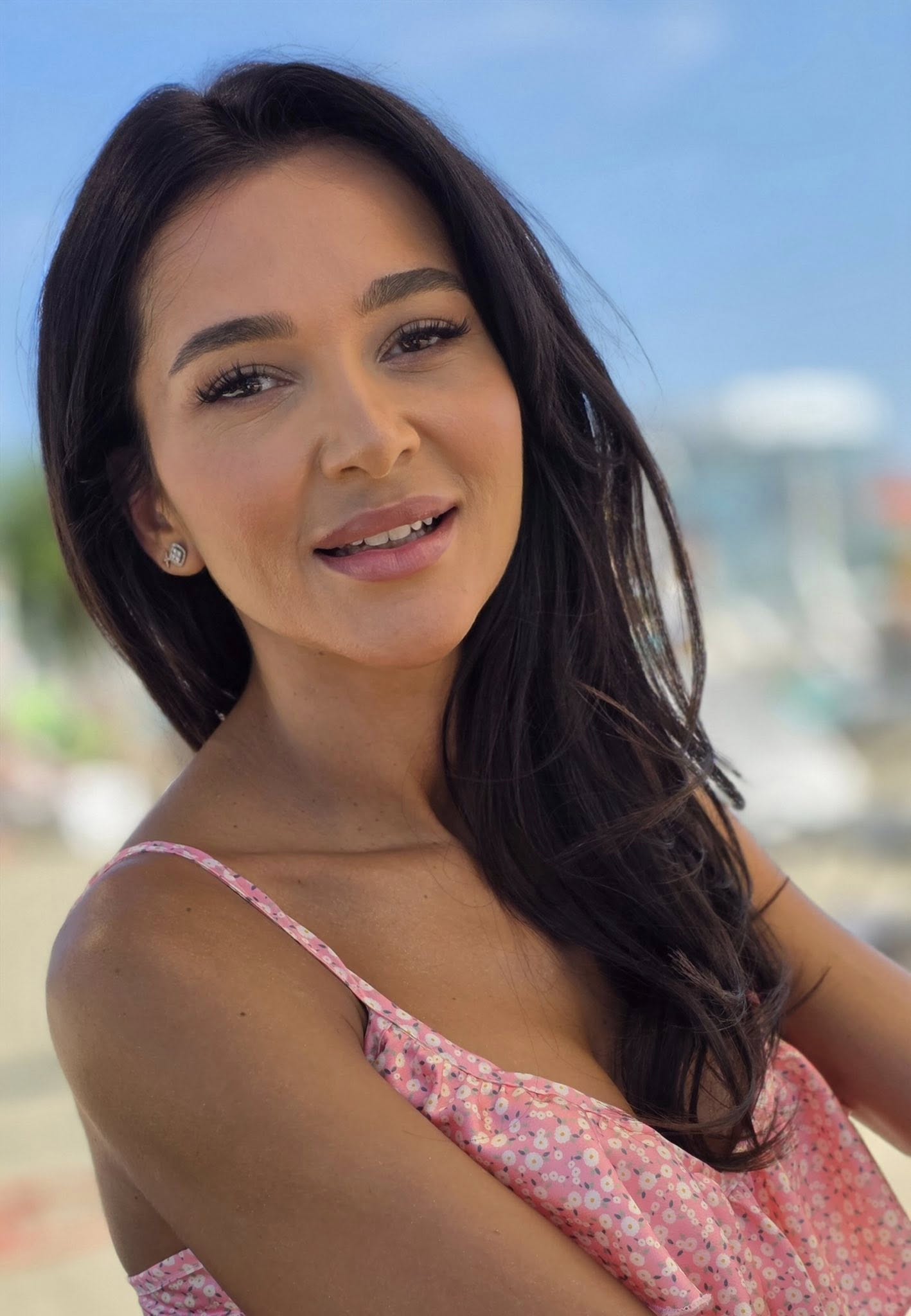 Ruxandra Luca z&acirc;mbitoare, făc&acirc;ndu-și un selfie pe plajă, &icirc;ntr-o rochiță roz cu flori, cu bretele subțiri, extrem de decoltată