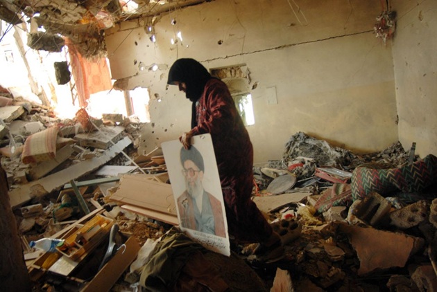 Persoană care stă printre dăr&acirc;măturile de sub care a scos un tablou cu liderul iranian Ali&nbsp;Khamenei