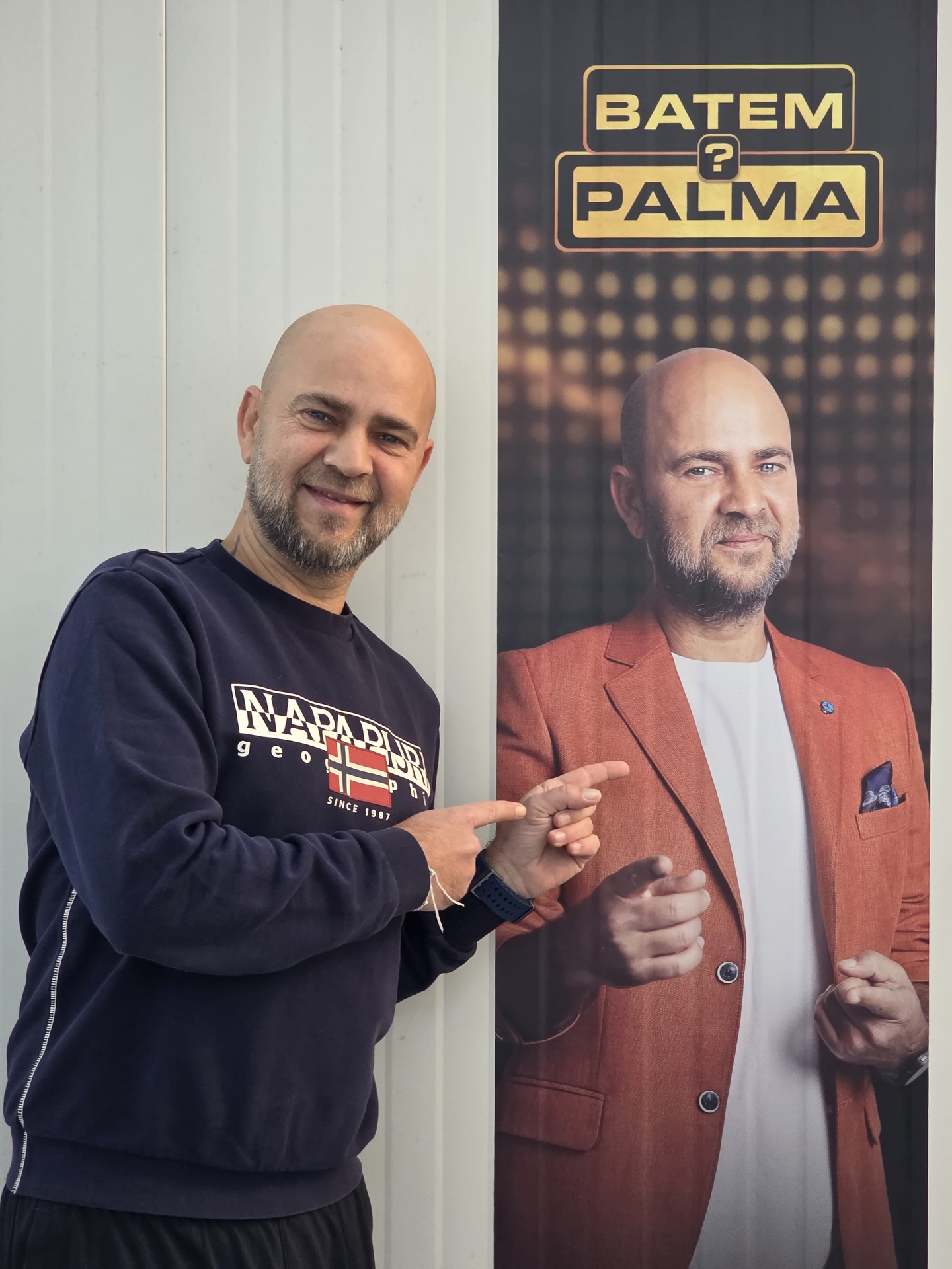 Cosmin Seleși z&acirc;mbitor, arăt&acirc;nd cu degetele afișul de promovare a emisiunii sale &bdquo;Batem Palma&rdquo; de la ProTV