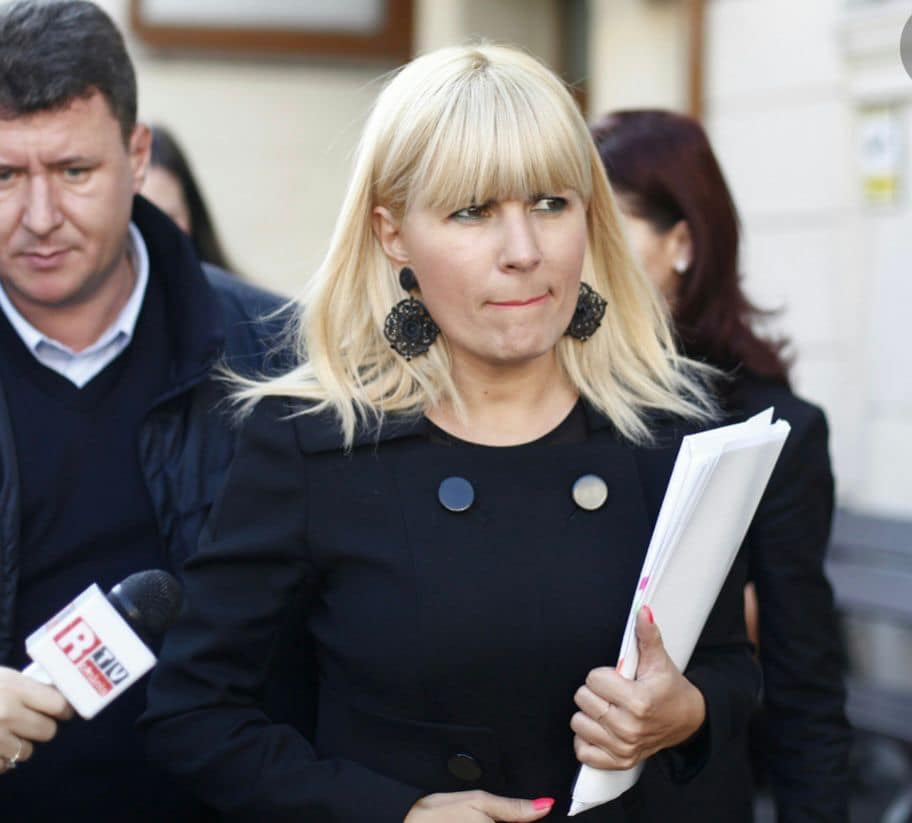 Elena Udrea &icirc;nconjurată de jurnaliști, &icirc;n timp ce mergea pe stradă cu un dosar &icirc;n m&acirc;nă, era &icirc;mbrăcată &icirc;n negru și purta cercei de mari dimensiuni asortați cu ținuta