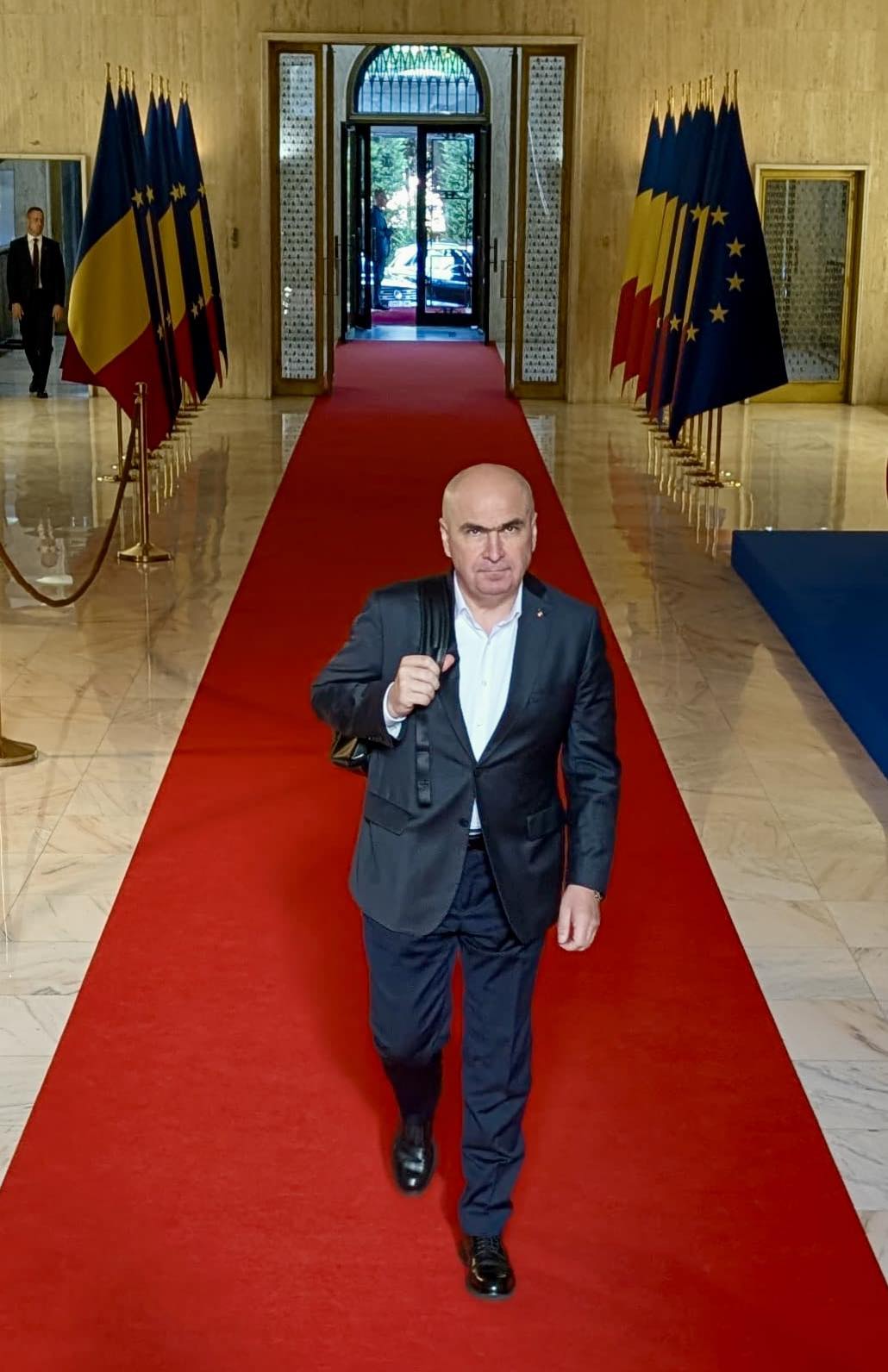 Ilie Bolojan pe covorul roșu din holul de la Palatul Victoria, &icirc;nconjurat de steaguri ale Rom&acirc;niei și ale UE