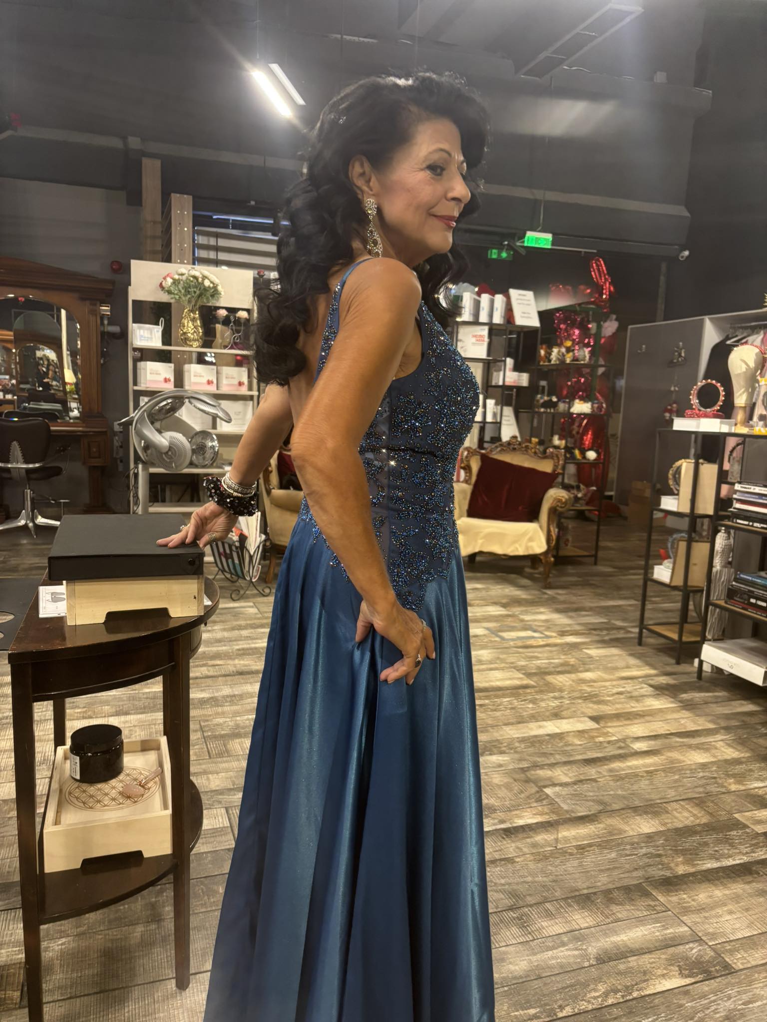 Fotografie din profil cu Elena C&acirc;rstea, &icirc;mbrăcată &icirc;n rochie de seară cu paiete, st&acirc;nd cu m&acirc;na &icirc;n șold, ca pe podium, coafată și machiată pentru un eveniment și purt&acirc;nd bijuterii de mari dimensiuni