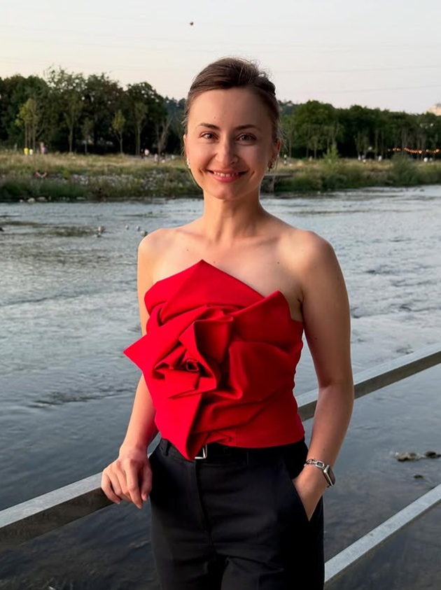 Aletta Mihai, pe malul unui lac, &icirc;mbrăcată &icirc;ntr-un top roșu cu umerii goi și trandafir suprafimensionat &icirc;n zona bustului