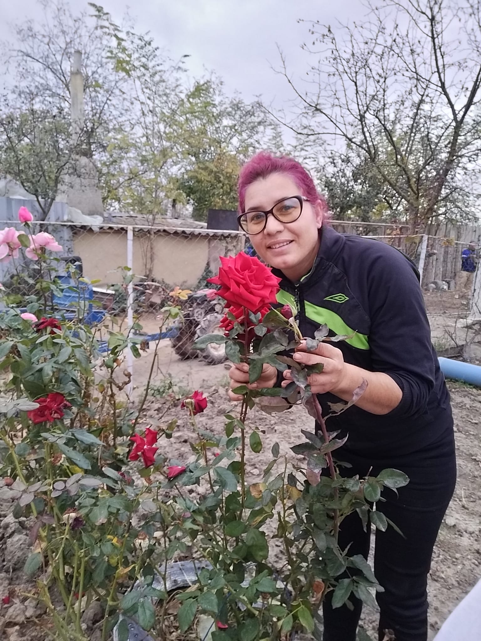 Elena Stroe &icirc;mbrăcată &icirc;ntr-un trening negru, părul vopsit &icirc;ntr-o nuanță de roșu, mirosind trandafirii din curte