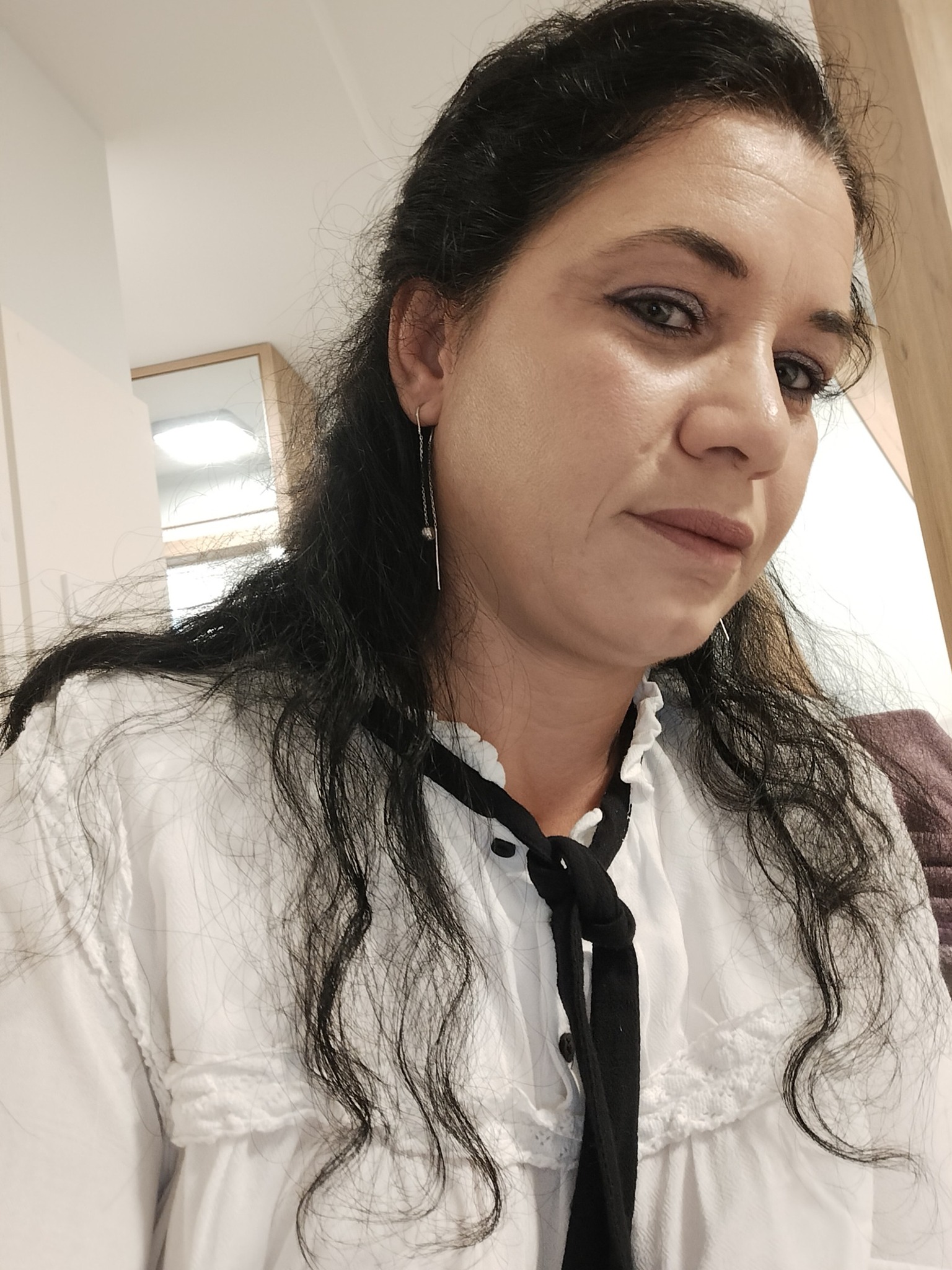 Elena Stroe &icirc;ntr-o cămașă albă cu șnur negru la g&acirc;t, cu părul pe jumătate prins la spate, făc&acirc;ndu-și un selfie