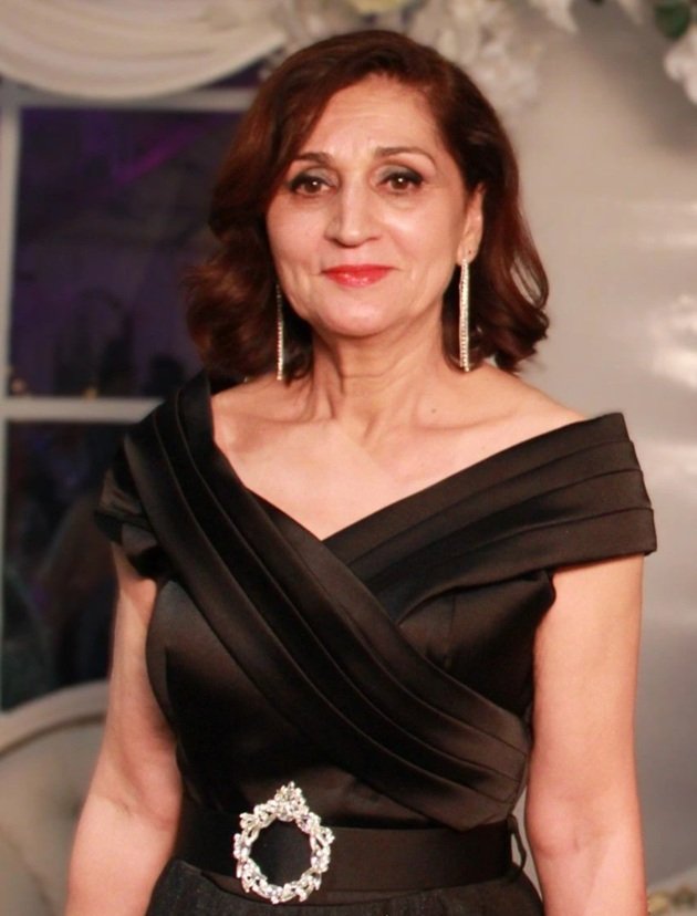 Dr. Liliana&nbsp;Forțu z&acirc;mbitoare, la o petrecere de seară, &icirc;mbrăcată &icirc;n rochie lungă, neagră, cu un accesoriu argintiu &icirc;n talie și cu cercei lungi cu pietre