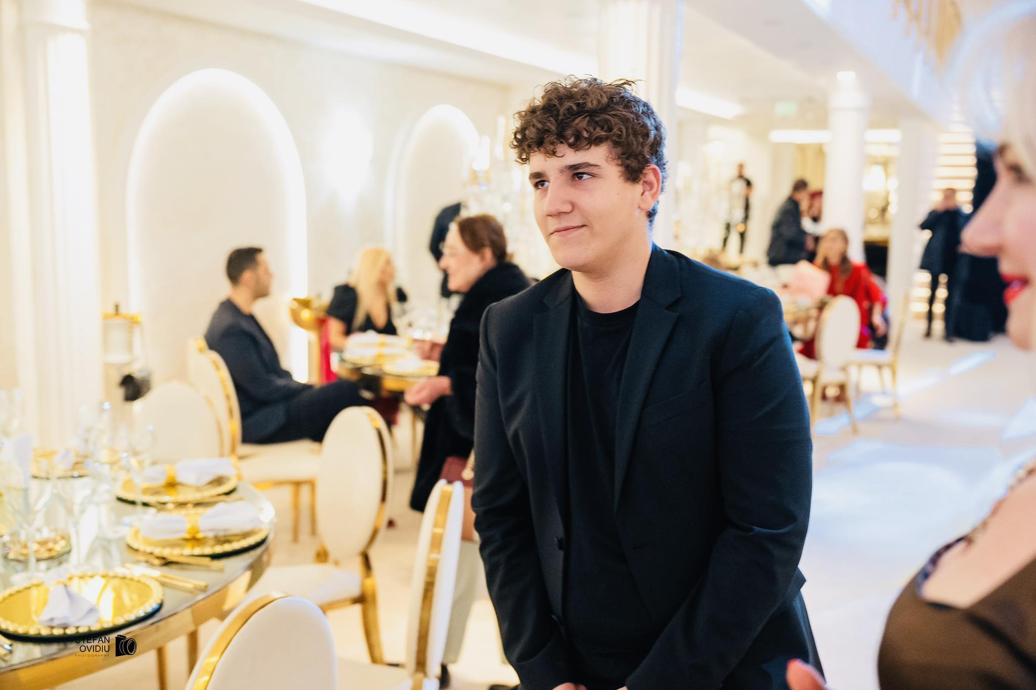 Dima, fiul Marei Bănică, la o petrecere la restaurant, &icirc;mbrăcat elegant &icirc;ntr-un costum negru, pe sub care avea un tricou negru