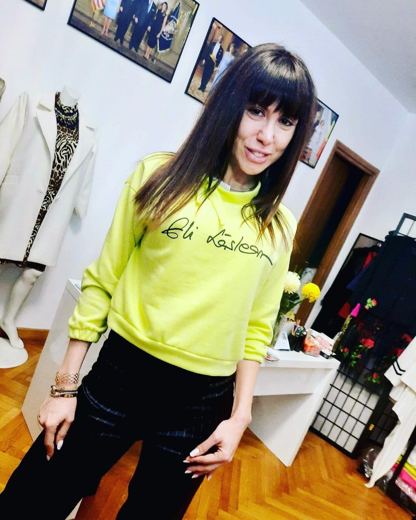 Denise Rifai z&acirc;mbitoare, fără machiaj, &icirc;ntr-un atelier de haine, purt&acirc;nd o bluză neon și pantaloni de culoare &icirc;nchisă
