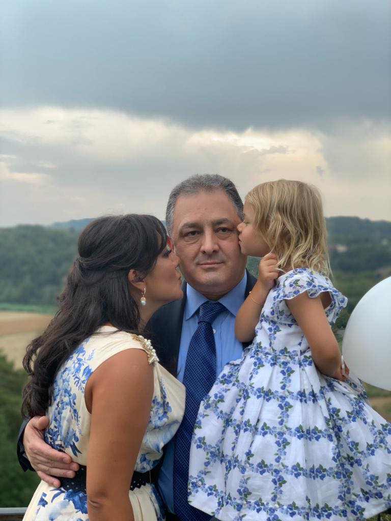 Oana Mizil și fiica ei, &icirc;mbrăcate asortat &icirc;n rochii albe cu flori albastre, sărut&acirc;ndu-l pe obraji pe Marian Vanghelie, tatăl copilei, care este &icirc;mbrăcat &icirc;ntr-un costum albastru și cămașă bleu