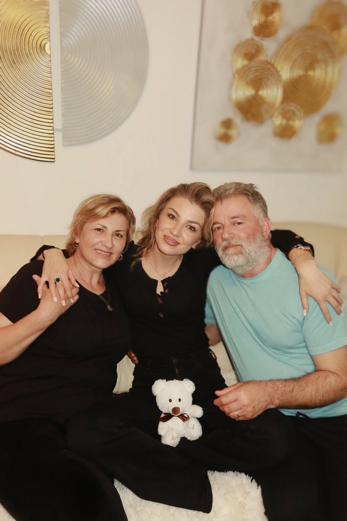 Codruța Filip țin&acirc;ndu-i de g&acirc;t pe părinții ei, &icirc;n timp ce stau toți pe aceeași canapea, iar ea ține &icirc;n brațe un ursuleț de pluș