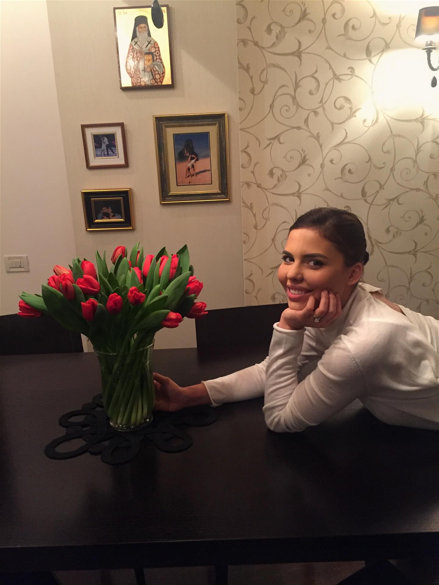 Andreea Popescu z&acirc;mbitoare, st&acirc;nd aplecată peste o masă mare &icirc;n centrul căreia se află o vază cu lalele