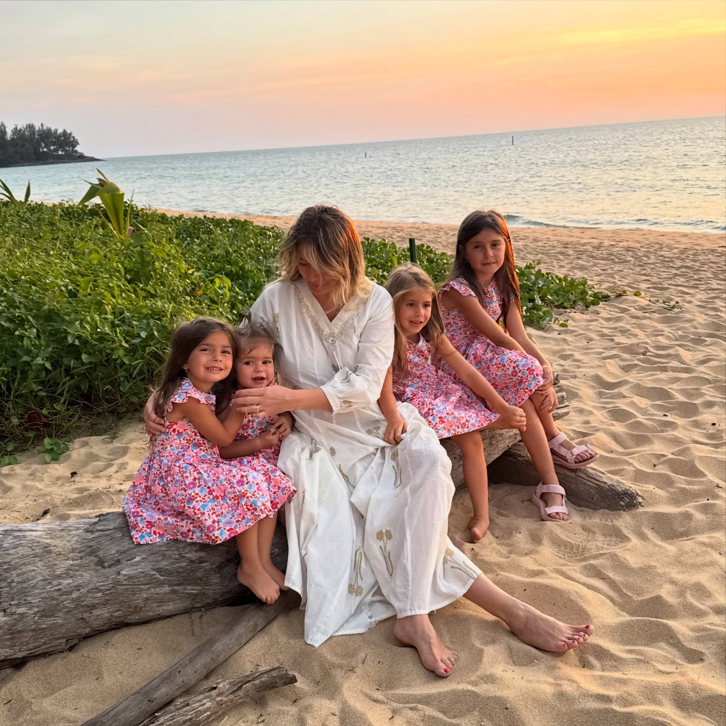 Laura Cosoi și fiicele sale, Rita, Vera, Lara și Aida, &icirc;mbrăcate &icirc;n rochii identice, st&acirc;nd l&acirc;ngă ea pe un buștean, pe plajă, &icirc;n timpul unei vacanțe