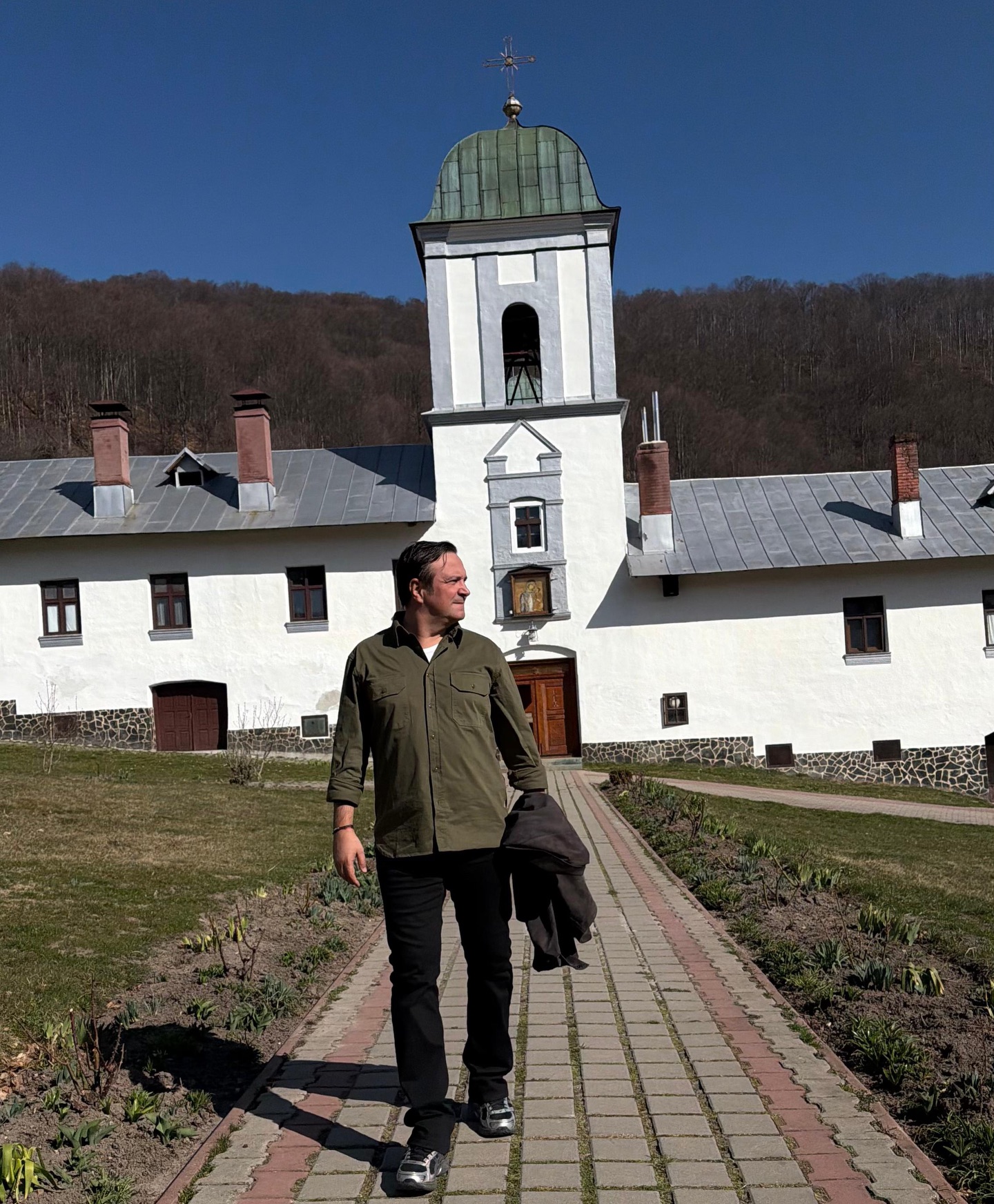 Daniel Buzdugan relaxat și liniștit pe aleea din fața Mănăstirii Frăsinei, țin&acirc;ndu-și geaca &icirc;n m&acirc;nă, &icirc;n timp ce privește &icirc;ntr-o parte.