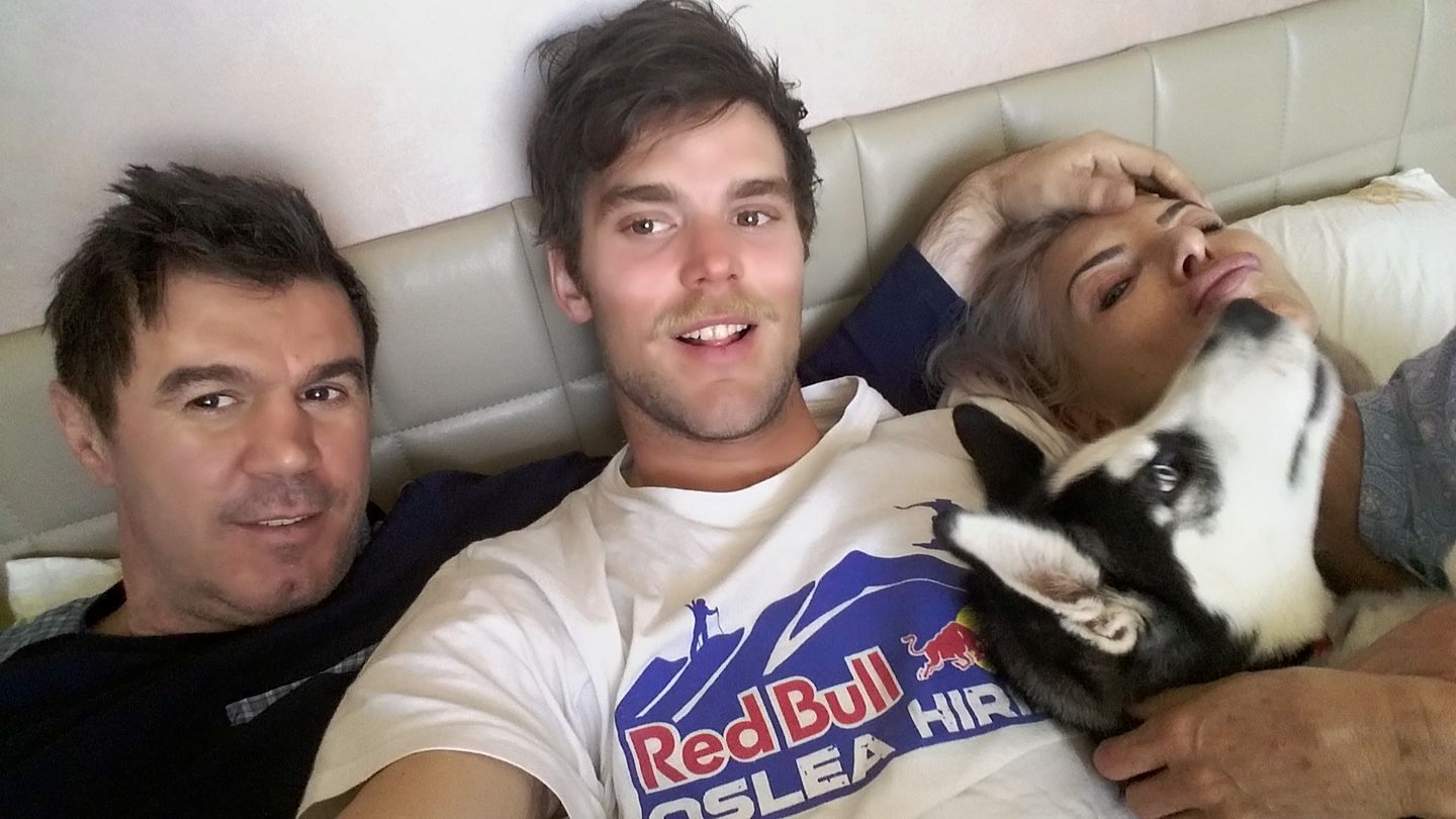 Mihai Leu z&acirc;mbitor, st&acirc;nd &icirc;n pat alături de soția sa, de fiul lor și de c&acirc;inele familiei, &icirc;n timp ce Marco face o fotografie cu toți patru