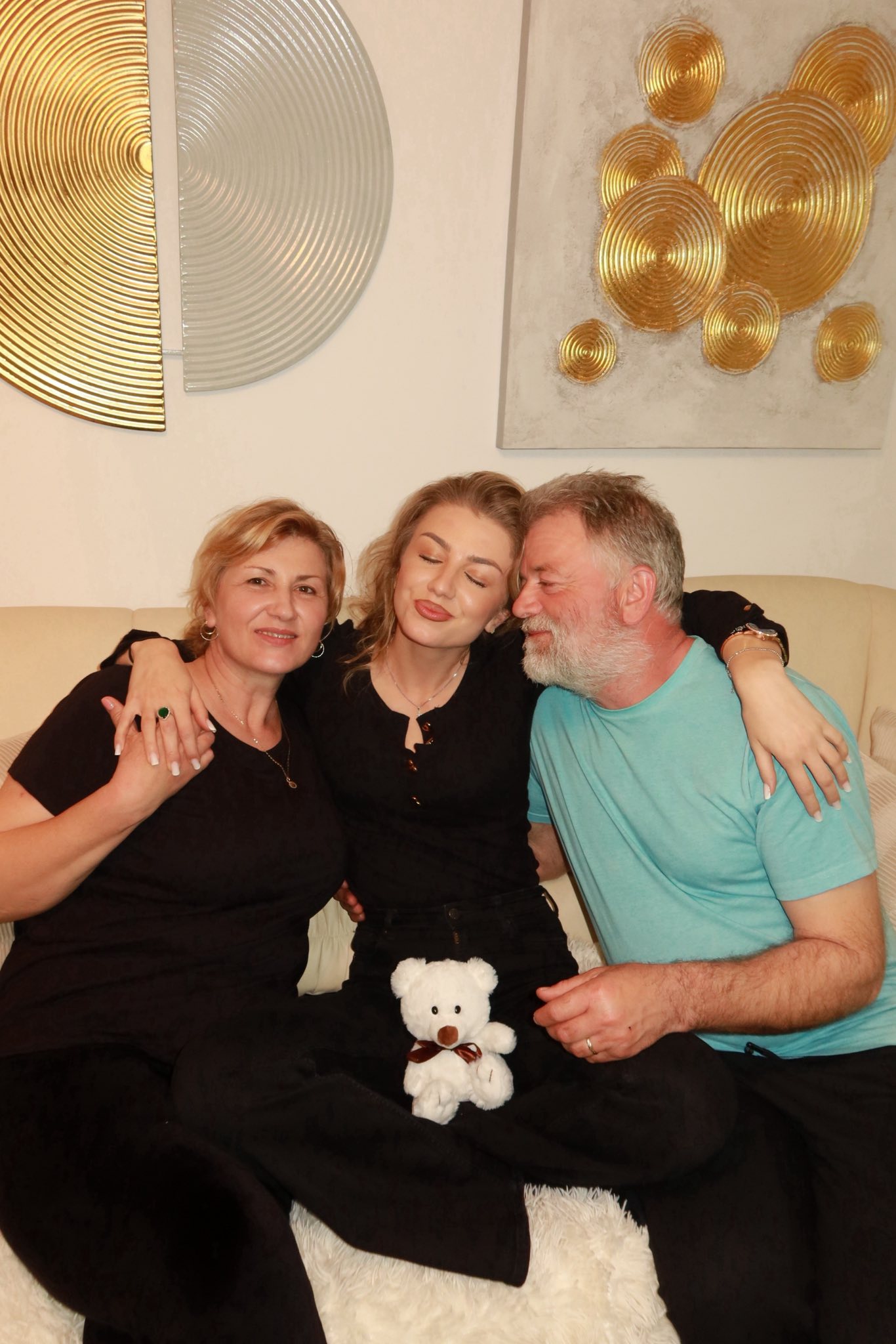 Codruța Filip st&acirc;nd pe canapea, alături de părinții ei, care o &icirc;mbrățișează str&acirc;ns